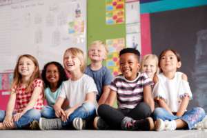 Group of diverse smiling children sitting on the classroom floor.